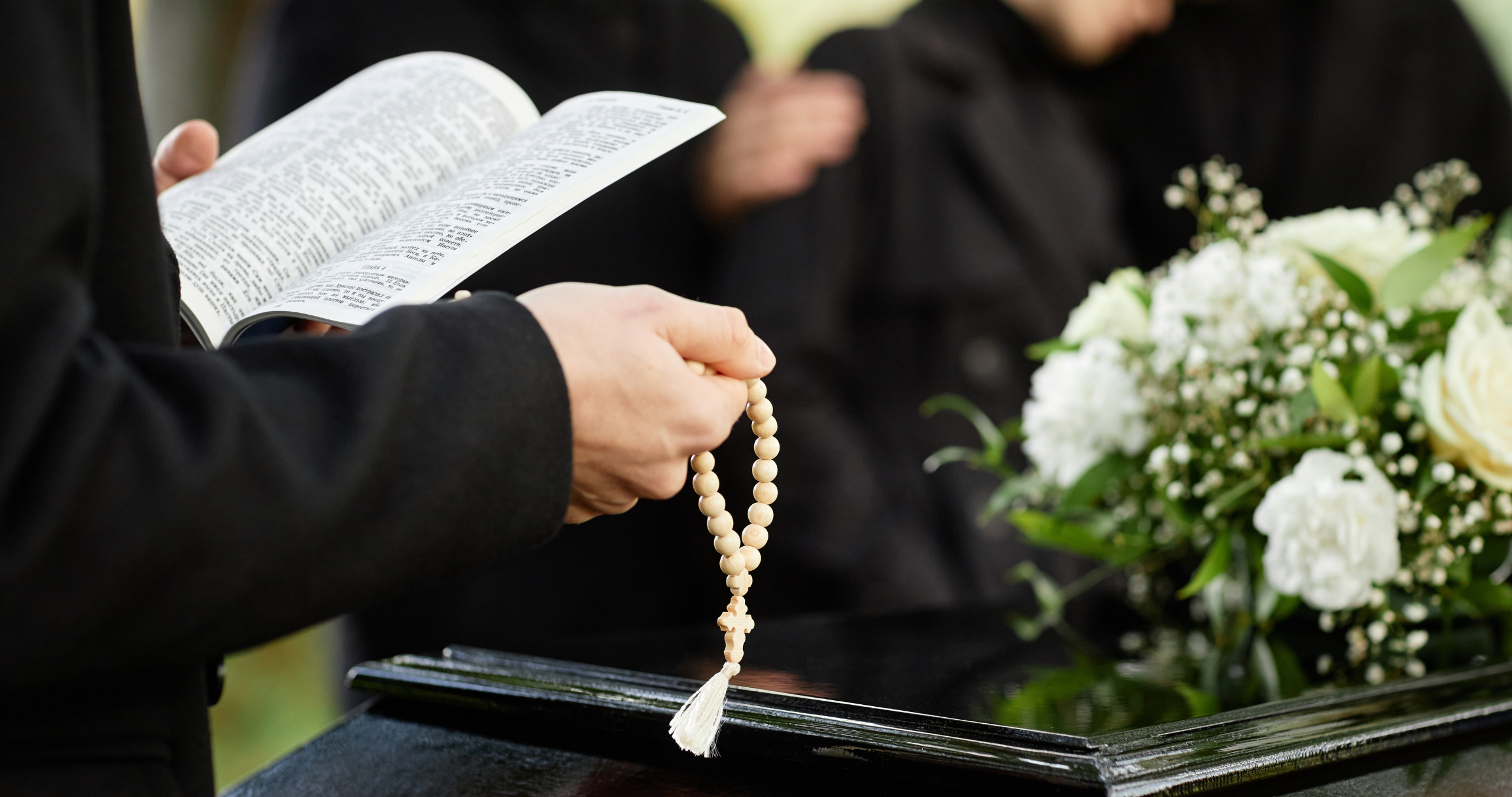 Close up of person in black praying at outdoor funeral and holding Bible with rosary, copy space