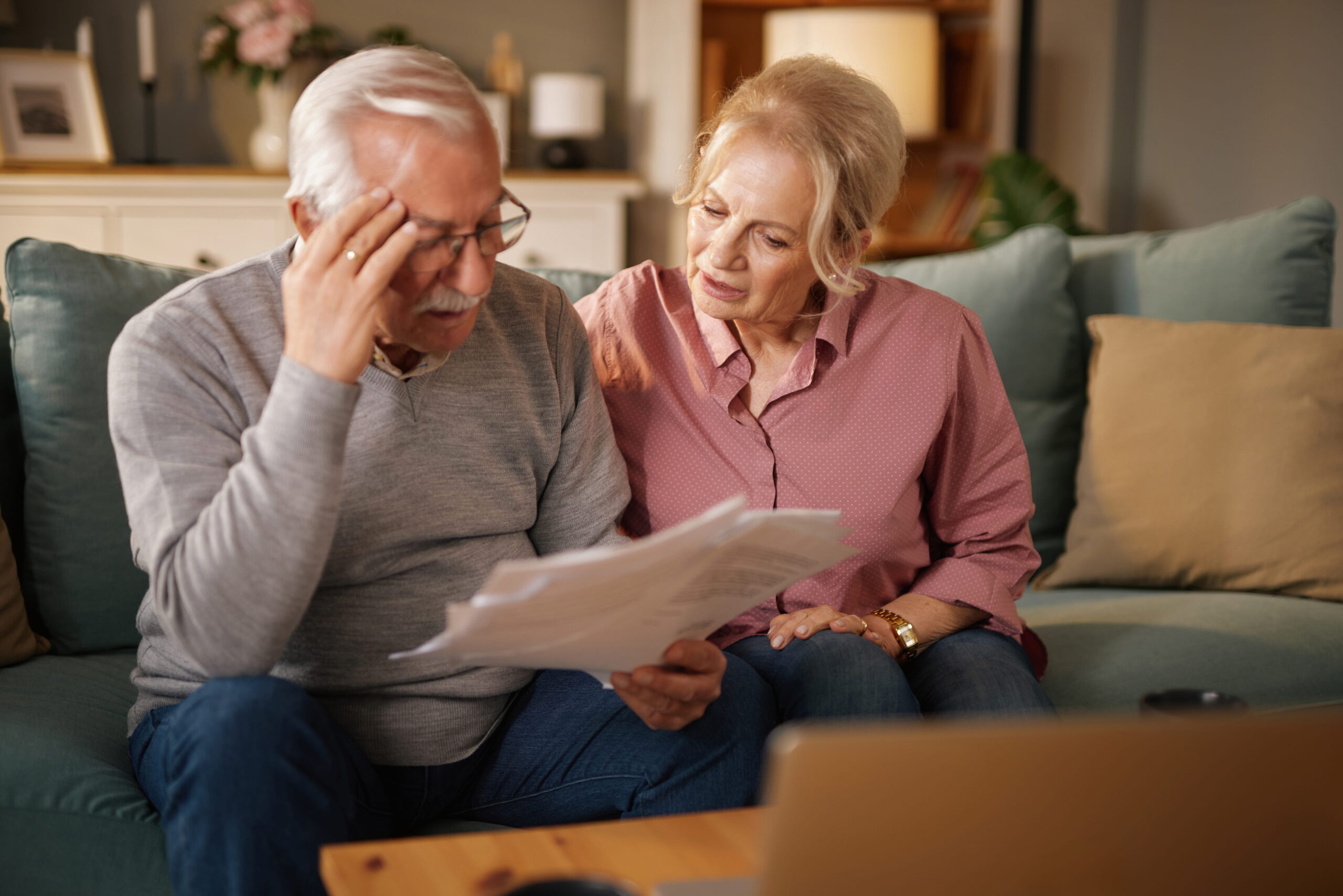 An older couple sits on their blue sofa while reviewing financial paperwork